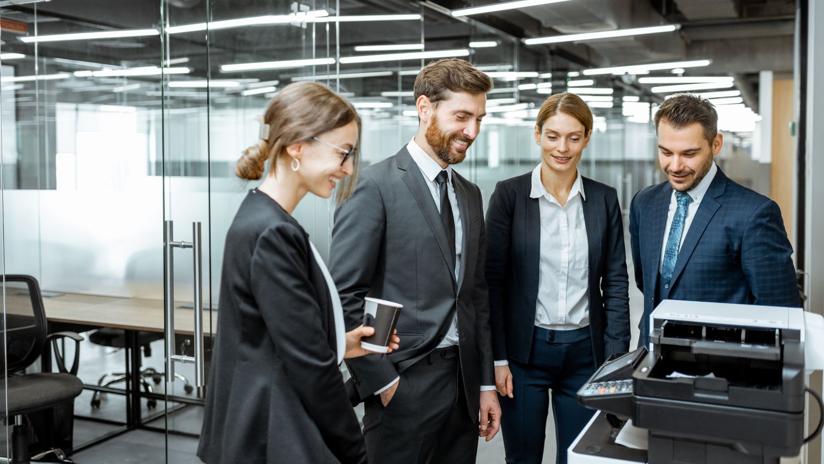 A group of people walking through an office space, passing by enterprise fax machines on the tables.